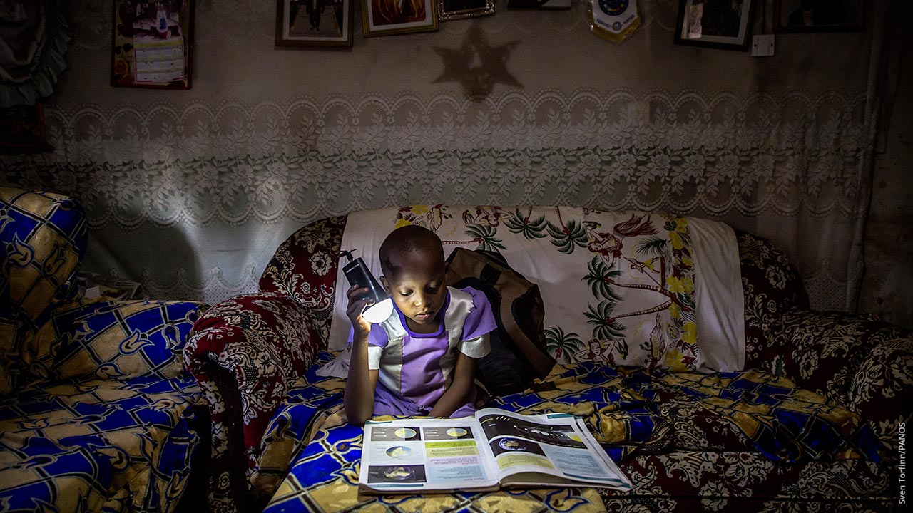 Tansanialainen tyttö opiskelee taskulampun valossa koulukirjaa